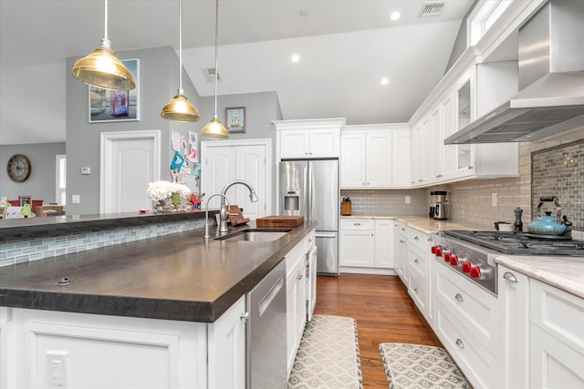 kitchen featuring a center island with sink, wall chimney exhaust hood, appliances with stainless steel finishes, hanging light fixtures, and white cabinetry