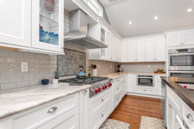 kitchen featuring glass insert cabinets, white cabinets, wall chimney range hood, and appliances with stainless steel finishes