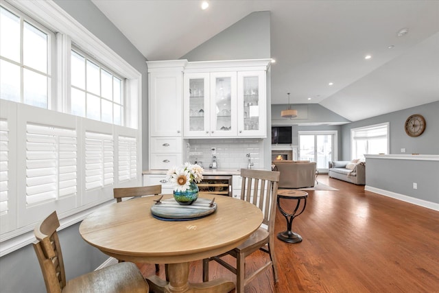 dining space with dark wood-style flooring, recessed lighting, vaulted ceiling, a lit fireplace, and baseboards