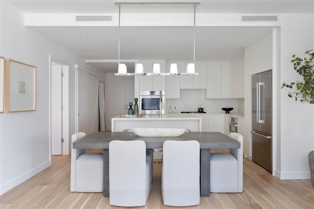 kitchen featuring high quality fridge, decorative light fixtures, visible vents, white cabinets, and a center island with sink