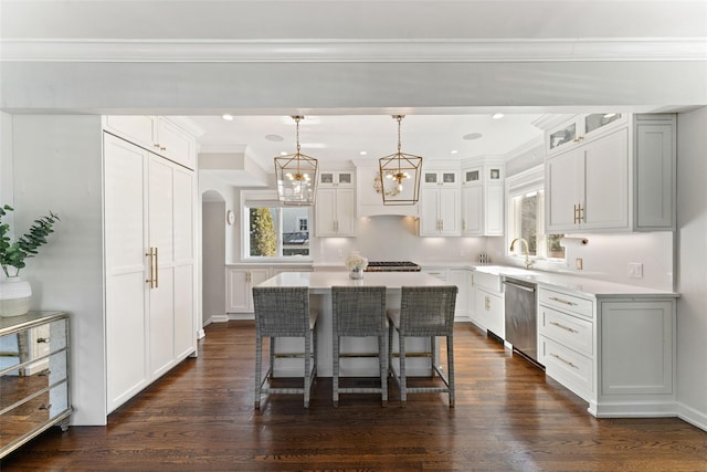 kitchen with arched walkways, a sink, stainless steel dishwasher, a center island, and dark wood-style floors