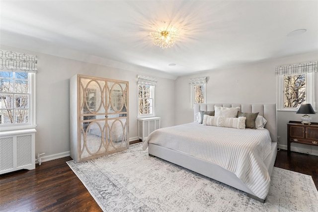 bedroom with radiator heating unit, multiple windows, baseboards, and wood finished floors