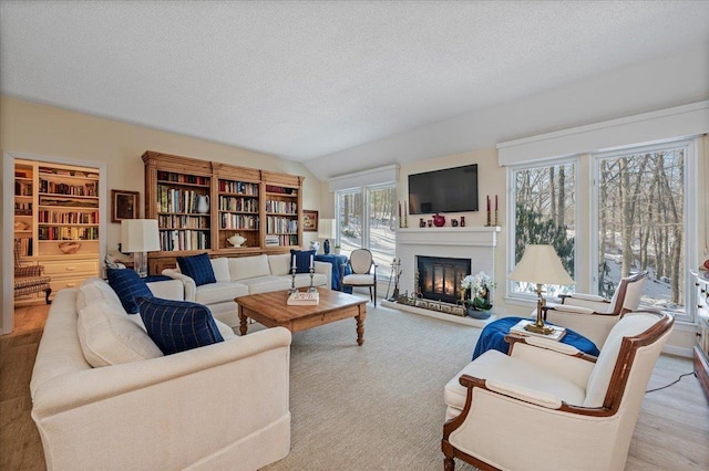 living room featuring a textured ceiling, a glass covered fireplace, and lofted ceiling