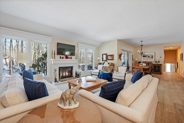 living room featuring a textured ceiling, light wood finished floors, a glass covered fireplace, and a notable chandelier