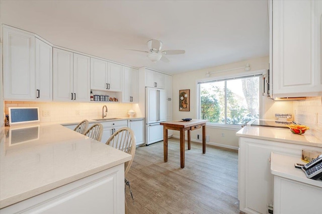 kitchen with light countertops, paneled refrigerator, a sink, and white cabinetry