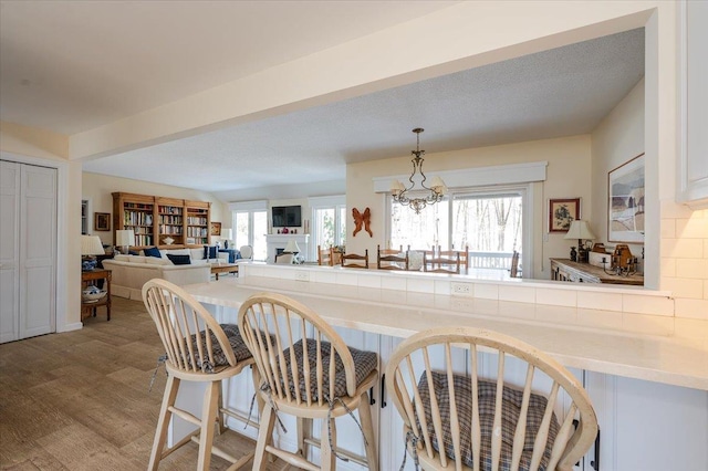 kitchen featuring a breakfast bar area, a fireplace, open floor plan, light countertops, and decorative light fixtures