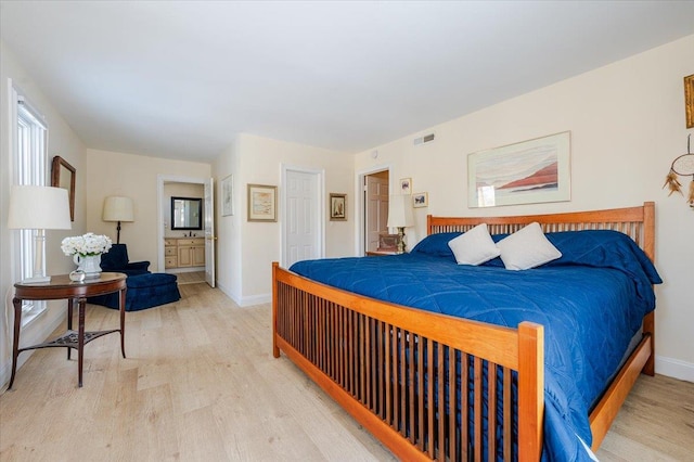 bedroom featuring ensuite bathroom, wood finished floors, visible vents, and baseboards