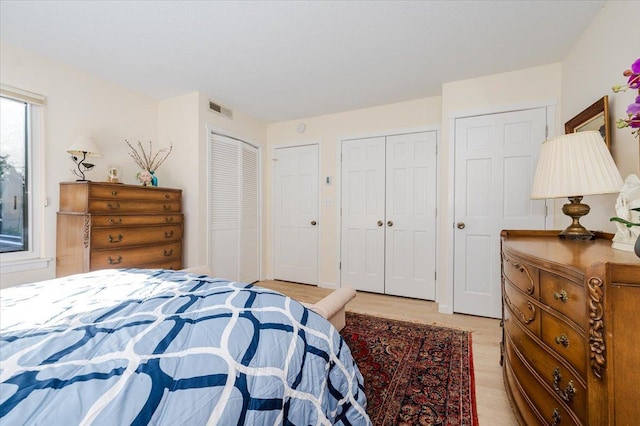 bedroom with light wood-type flooring, visible vents, and multiple closets