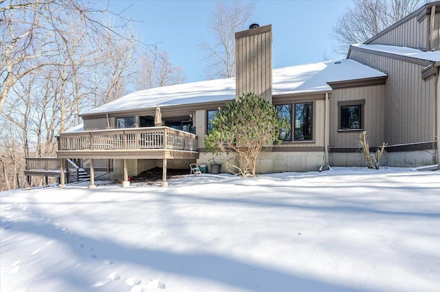 snow covered house featuring a deck and a chimney