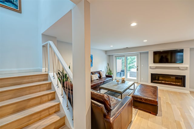 living room with light wood finished floors, recessed lighting, stairway, and a glass covered fireplace