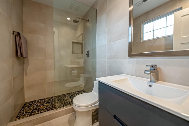 full bath featuring tile walls, visible vents, toilet, vanity, and walk in shower