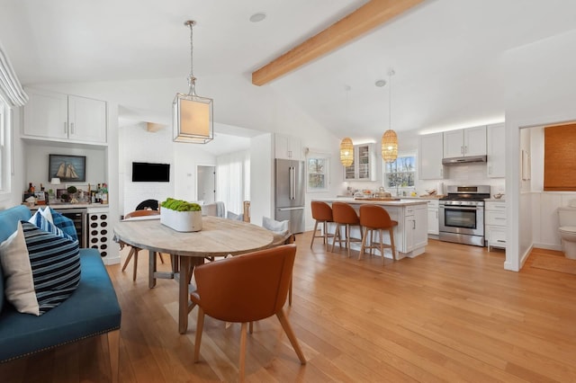 dining space featuring high vaulted ceiling, beamed ceiling, light wood-type flooring, and a fireplace