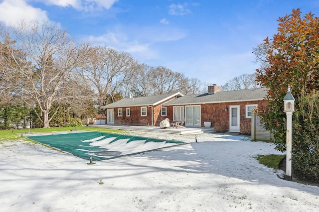 view of front facade with a patio area, a covered pool, and a chimney