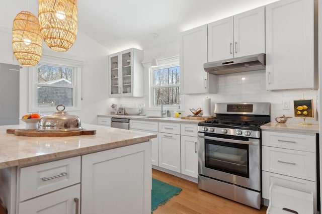 kitchen featuring under cabinet range hood, white cabinets, appliances with stainless steel finishes, glass insert cabinets, and pendant lighting