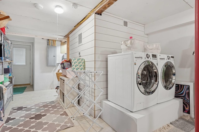 clothes washing area featuring laundry area, wood walls, washer and clothes dryer, and electric panel