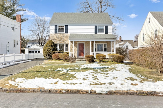 view of front of house featuring stone siding, fence, a porch, and roof with shingles