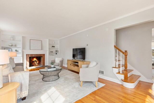 living room with a fireplace, wood finished floors, visible vents, stairs, and ornamental molding