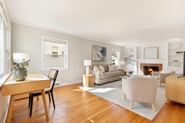 living area with built in shelves, light wood-style flooring, baseboards, ornamental molding, and a brick fireplace