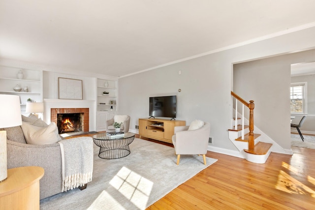 living area featuring ornamental molding, a brick fireplace, wood finished floors, baseboards, and stairs