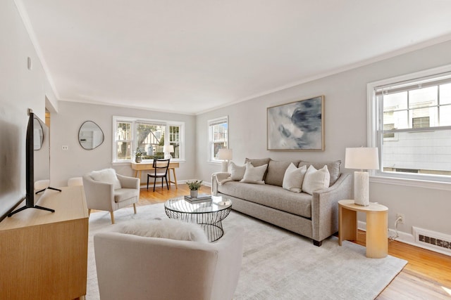 living room with ornamental molding, visible vents, light wood-style flooring, and baseboards