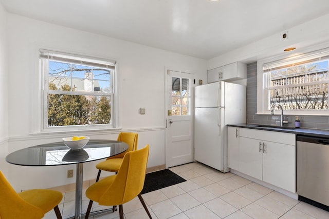 kitchen featuring dishwasher, dark countertops, freestanding refrigerator, and white cabinets