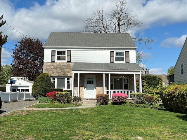 traditional-style house with a porch, a front yard, stone siding, and a shingled roof