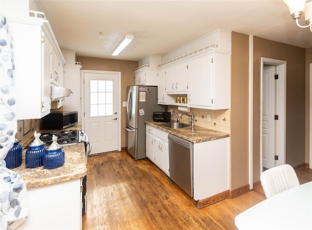 kitchen featuring stainless steel appliances, backsplash, white cabinetry, a sink, and light wood-type flooring