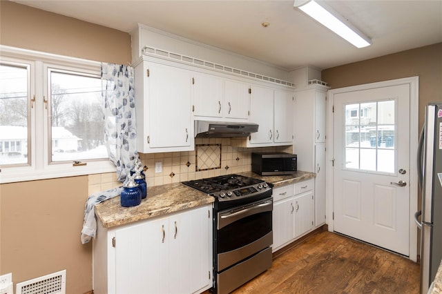 kitchen with tasteful backsplash, visible vents, dark wood finished floors, stainless steel appliances, and under cabinet range hood