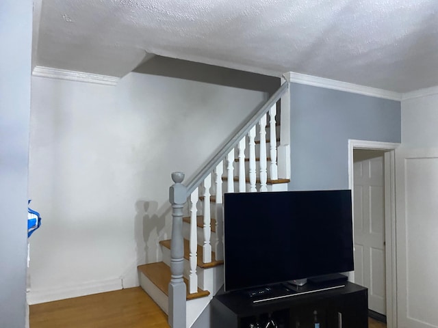 staircase with crown molding, wood-type flooring, and a textured ceiling