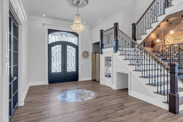 foyer featuring dark wood-style floors, french doors, an inviting chandelier, and crown molding