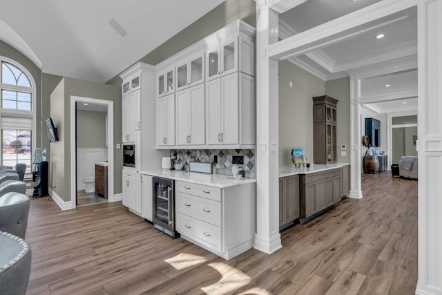 kitchen with beverage cooler, white cabinets, light stone counters, glass insert cabinets, and crown molding