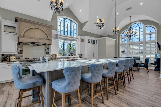 kitchen featuring pendant lighting, a kitchen island with sink, light wood finished floors, glass insert cabinets, and an inviting chandelier