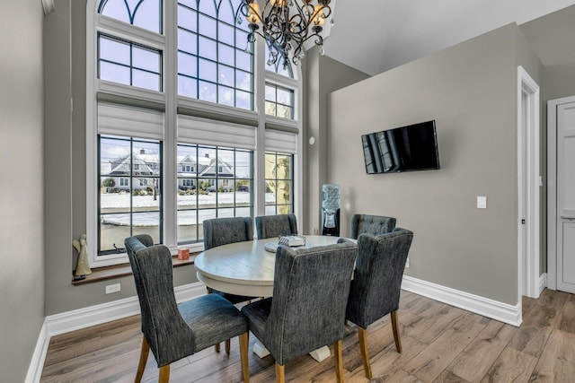 dining area featuring a chandelier, a high ceiling, baseboards, and wood finished floors