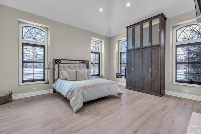 bedroom with a towering ceiling, light wood finished floors, and baseboards