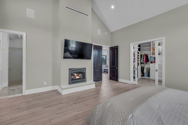 bedroom featuring a walk in closet, french doors, light wood finished floors, a glass covered fireplace, and baseboards