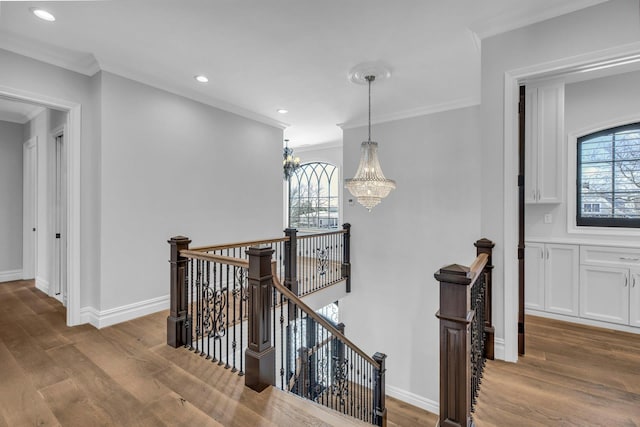 hallway featuring crown molding, a notable chandelier, light wood-style flooring, and an upstairs landing