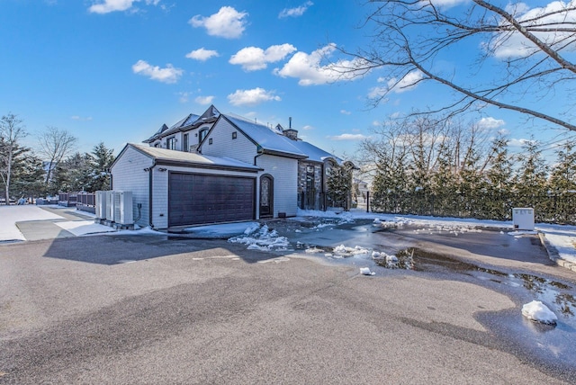 view of front of house featuring an attached garage, driveway, a chimney, and cooling unit