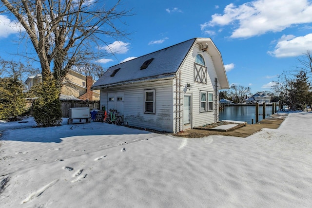 view of snow covered exterior with a water view, fence, and a gambrel roof