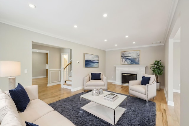 living area with crown molding, visible vents, a fireplace with flush hearth, light wood-style floors, and baseboards