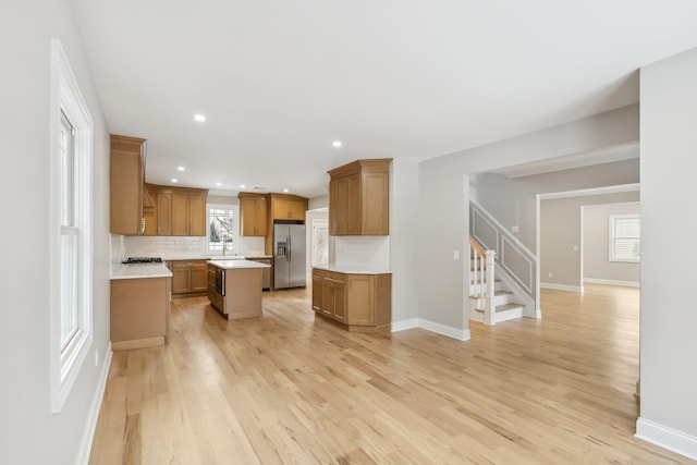 kitchen featuring a center island, light countertops, a sink, light wood-type flooring, and stainless steel fridge with ice dispenser