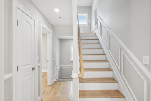 staircase featuring recessed lighting, a decorative wall, wood finished floors, and wainscoting
