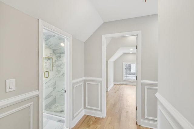 interior space with lofted ceiling, a wainscoted wall, light wood-type flooring, and a decorative wall