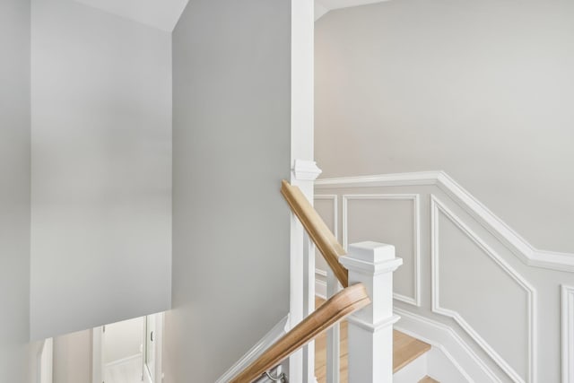 stairway with lofted ceiling, wainscoting, and a decorative wall