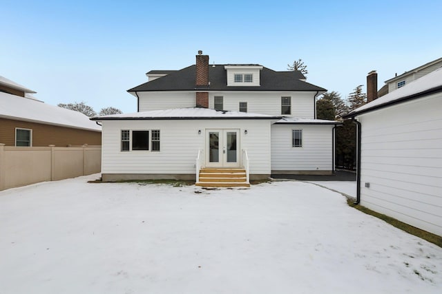 snow covered back of property with french doors, fence, and a chimney