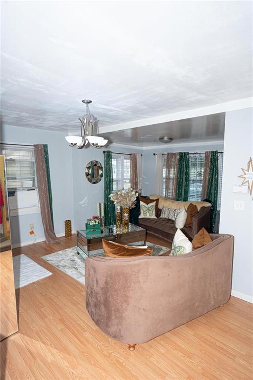 living area with baseboards, light wood-type flooring, and a notable chandelier