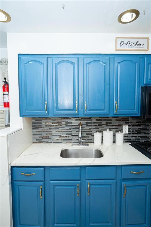 kitchen featuring blue cabinets, light stone countertops, tasteful backsplash, and a sink