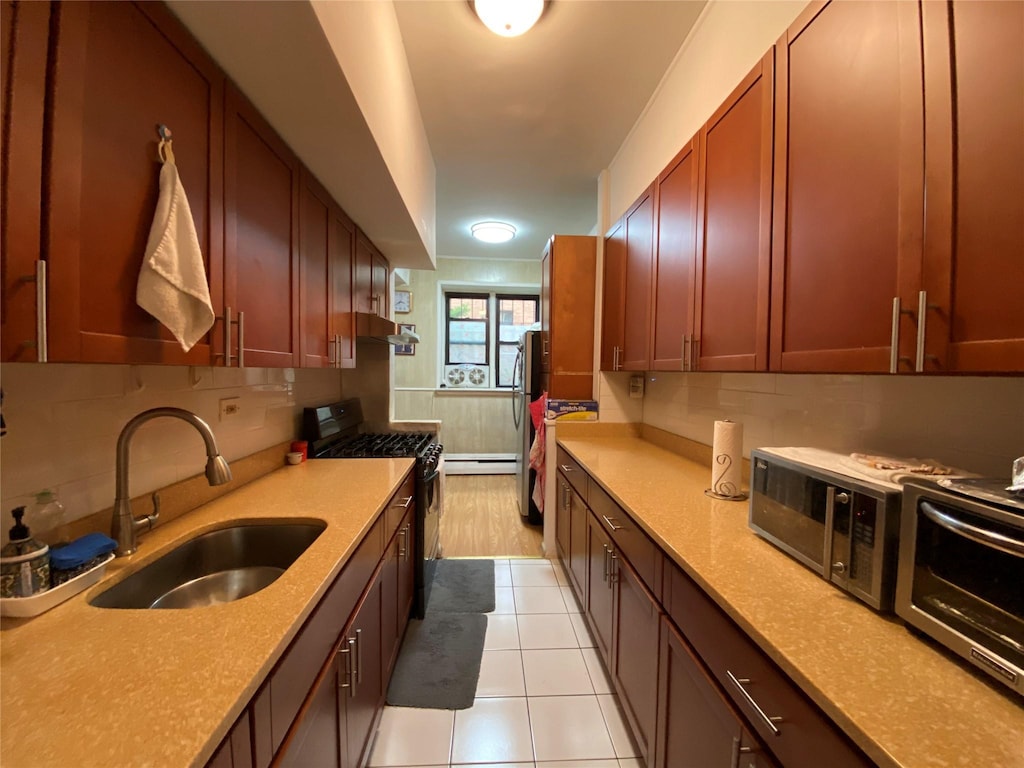 kitchen featuring black gas range oven, sink, stainless steel refrigerator, tasteful backsplash, and light tile patterned flooring