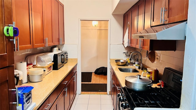 kitchen with a sink, under cabinet range hood, light countertops, and stainless steel range with gas stovetop