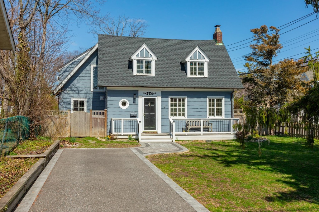cape cod home featuring a chimney, fence, roof with shingles, and a front yard