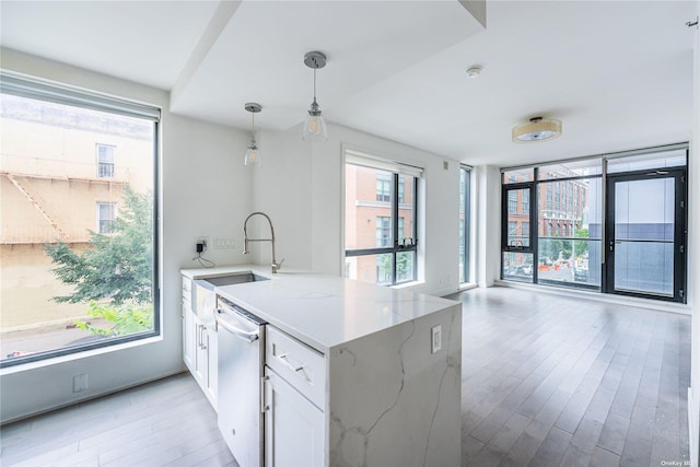 kitchen with pendant lighting, sink, dishwasher, light stone countertops, and white cabinets